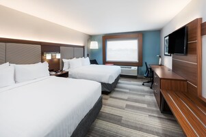 Habitación de hotel con dos camas, un escritorio, un televisor y un ventanal amplio.