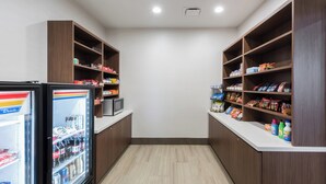 Et lille, overskueligt tekøkken med et køleskab fyldt med drikkevarer, en mikrobølgeovn og hylder med snacks og krydderier.