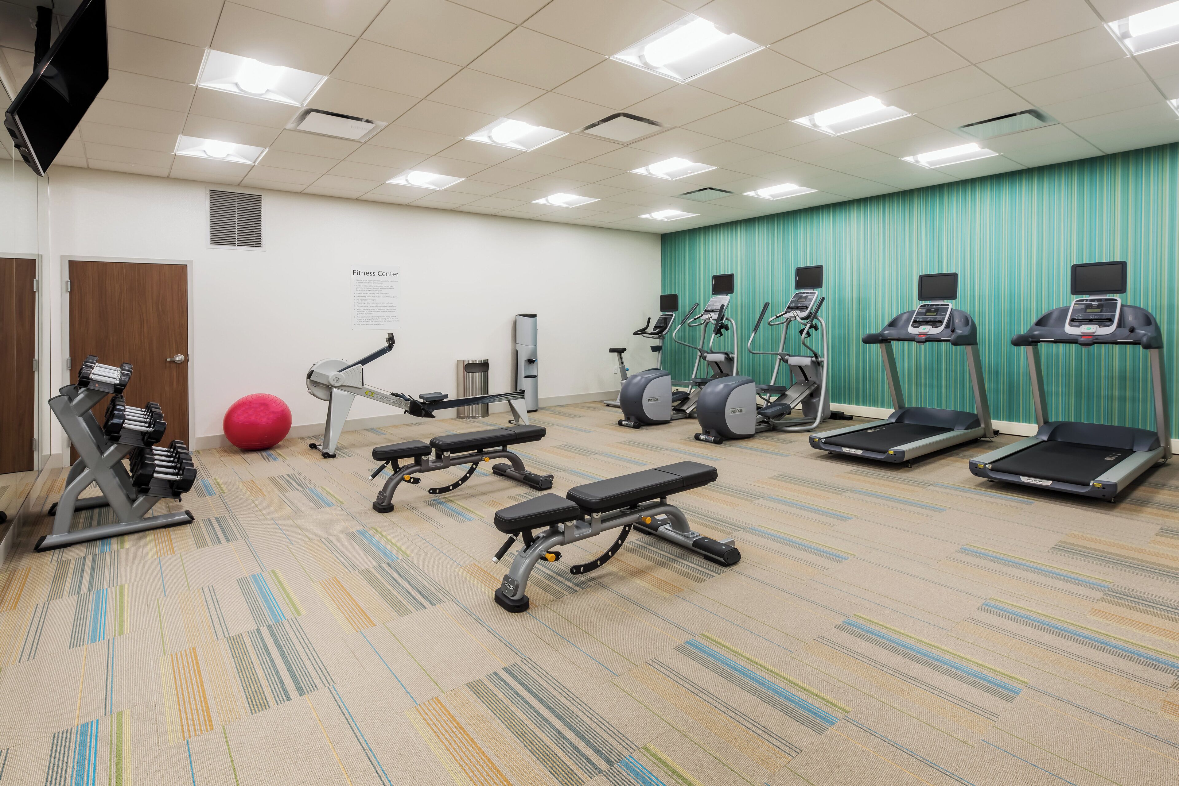 Un gimnasio equipado con cintas de correr, elípticas, una banca y mancuernas.