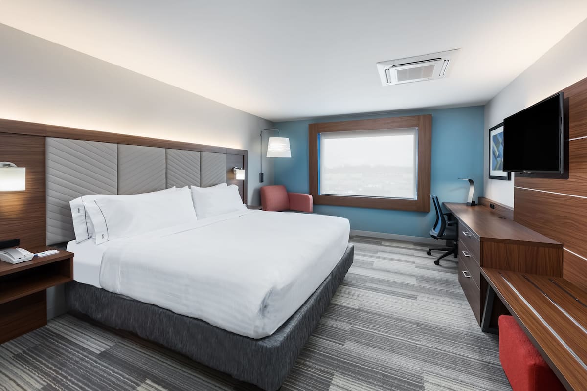 Una habitació d'hotel moderna amb un llit gran, una taula de treball, una cadira, un televisor i una finestra amb vista a la ciutat.