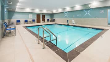 A swimming pool with a metal ladder, lounge chairs, and a clock on the wall.