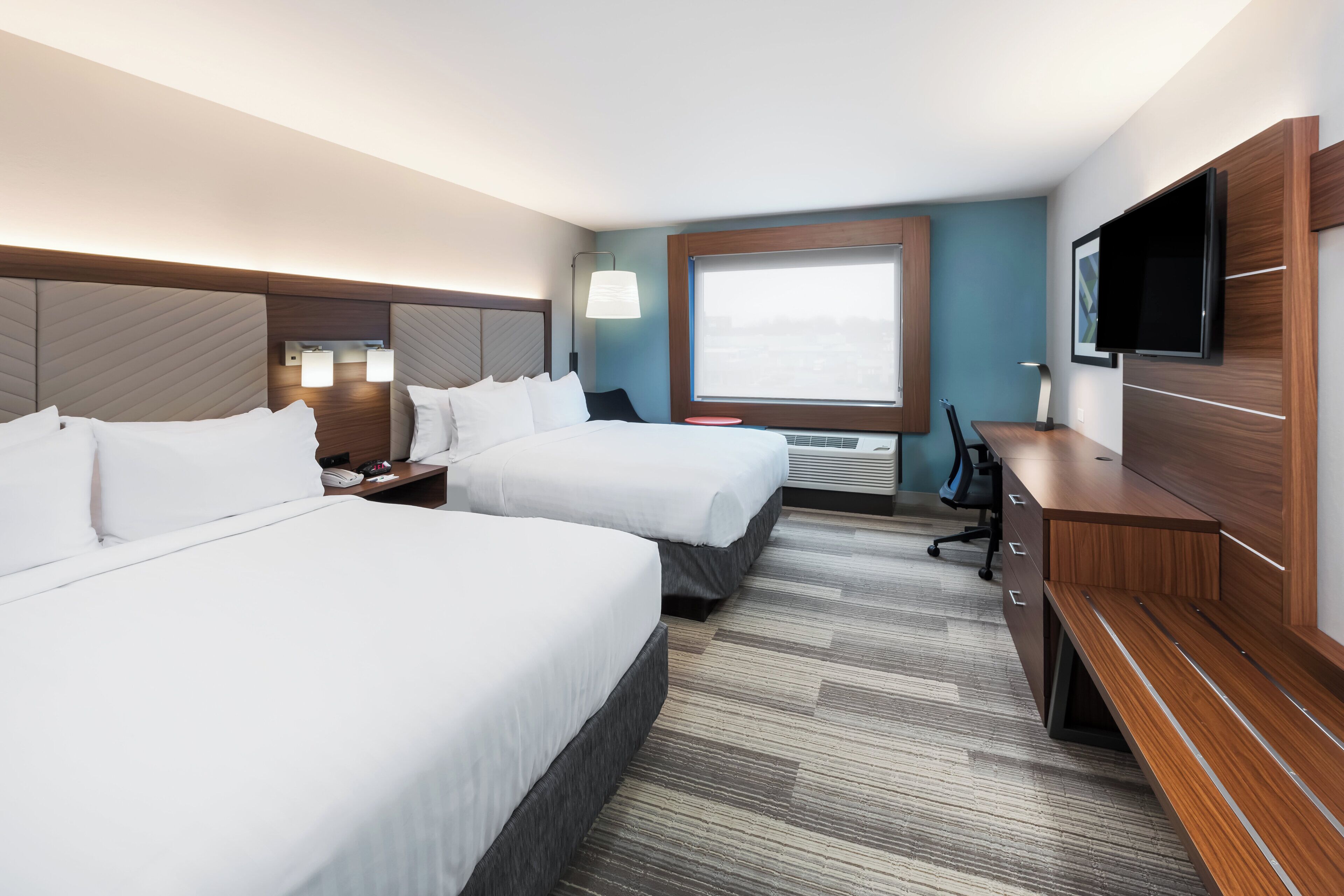 Ett hotellrum med två sängar, ett skrivbord, en stol, en TV och ett fönster med utsikt.