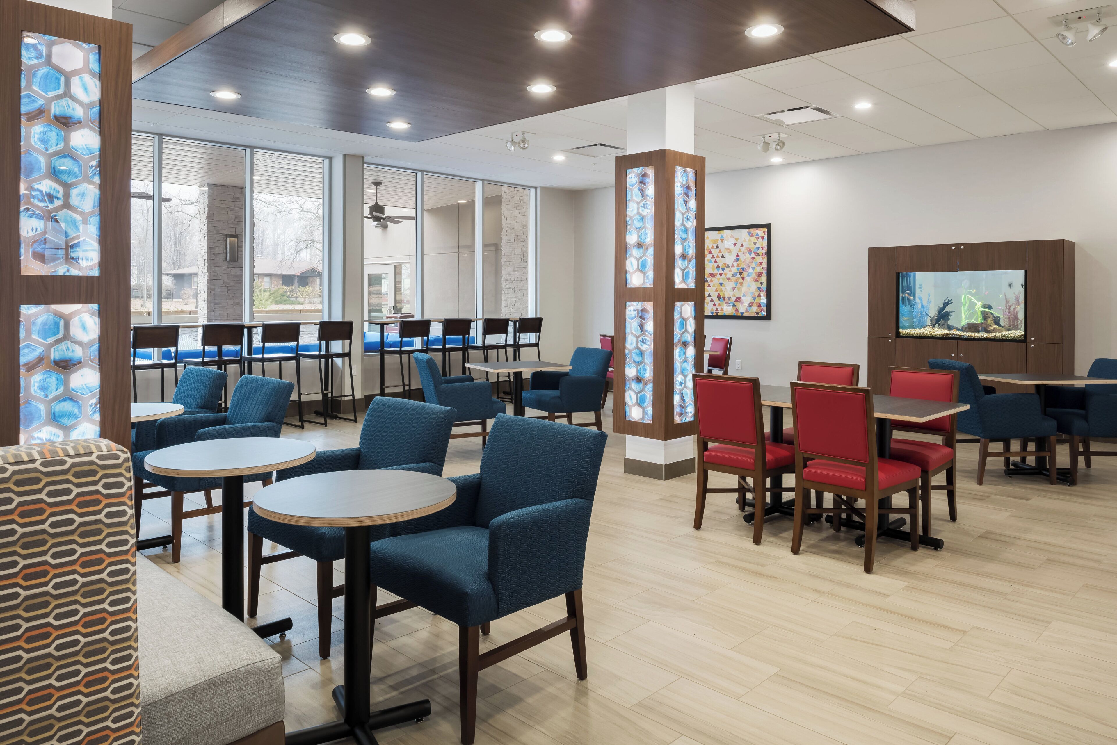 A modern dining area with blue and red chairs, round tables, and a large aquarium on the wall.