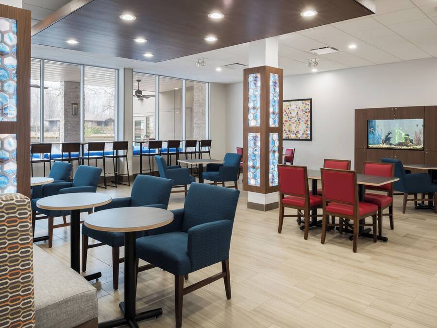 A modern dining area with blue and red chairs, round tables, and a large aquarium on the wall.