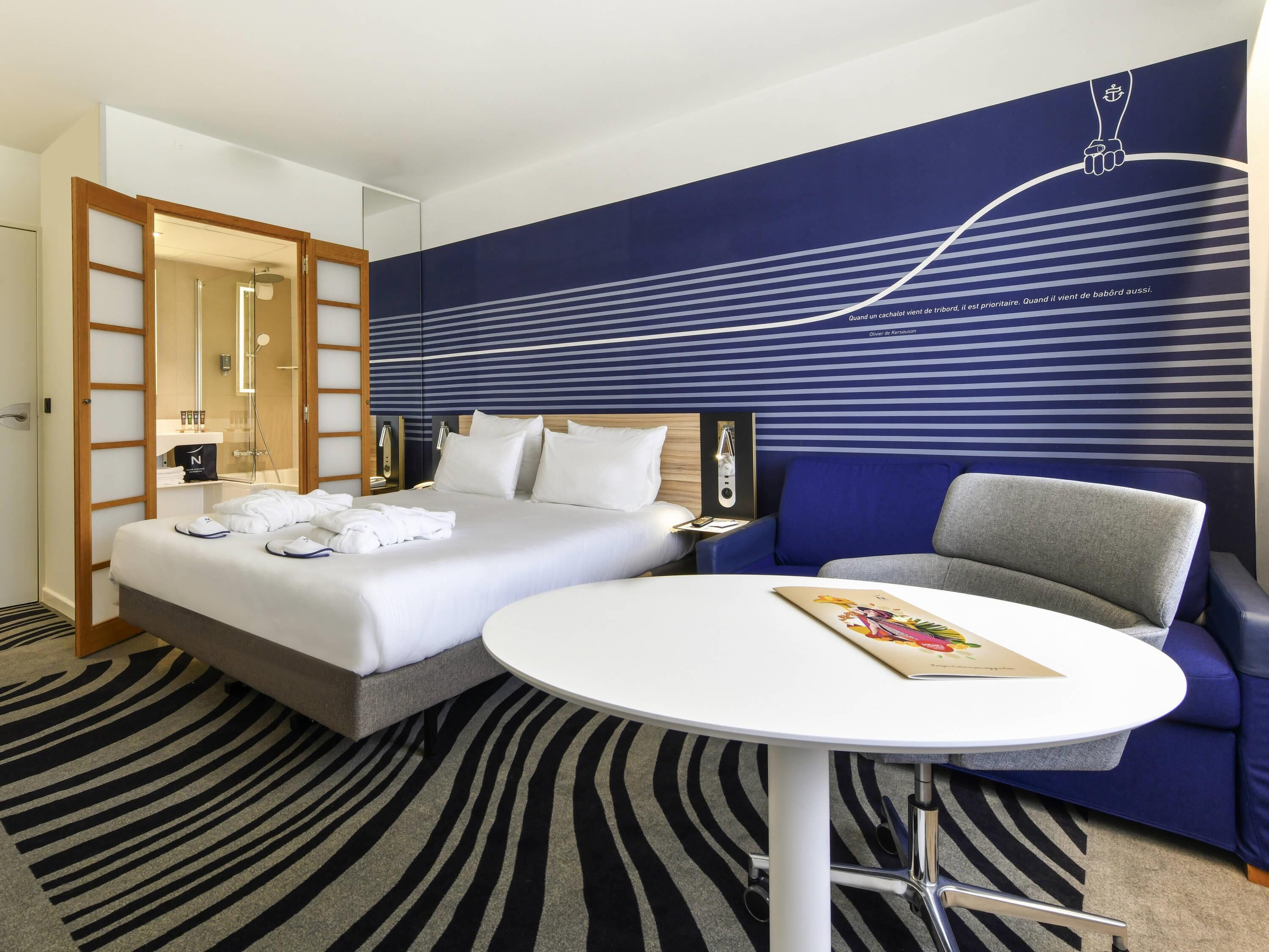 Habitación de hotel con cama, mesita de noche, una silla, una mesa redonda y una pared con estampado a rayas.