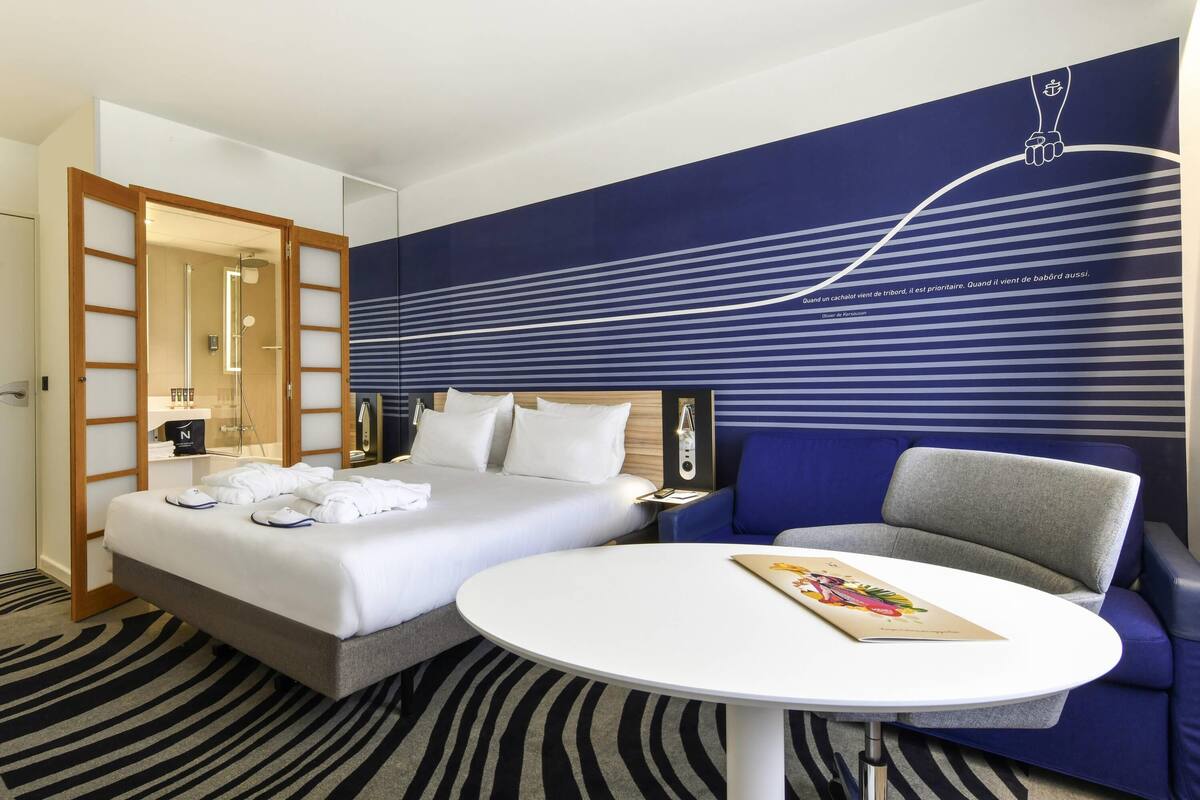 Habitación de hotel con cama, mesita de noche, una silla, una mesa redonda y una pared con estampado a rayas.