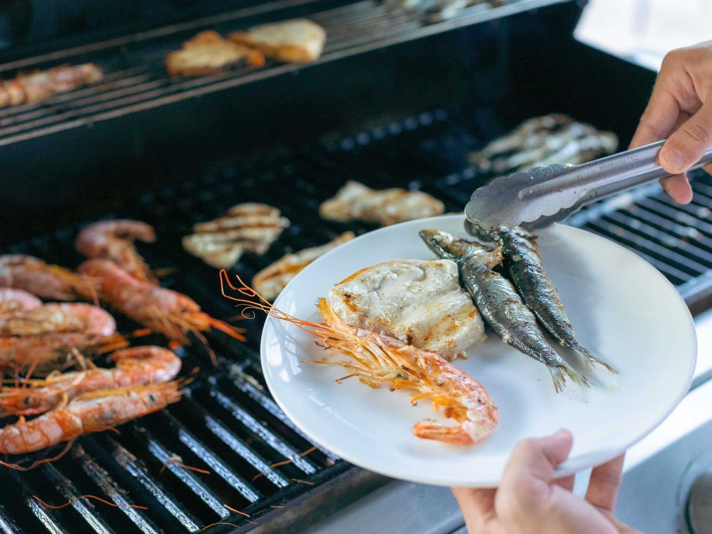 A person grilling seafood and shrimp on a barbecue.