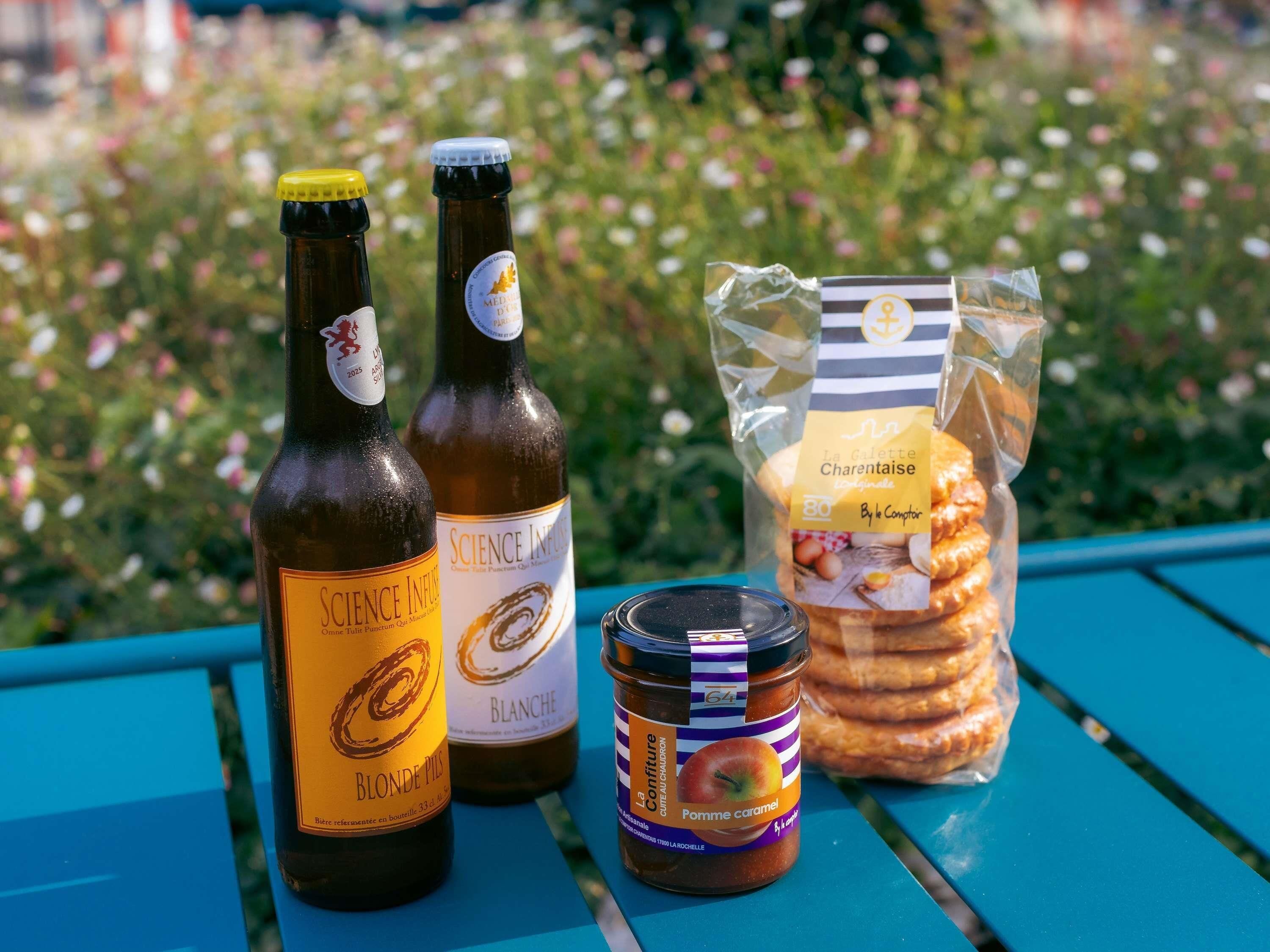Two bottles of wine, a jar of jam, and a bag of biscuits on a table with a blue surface.