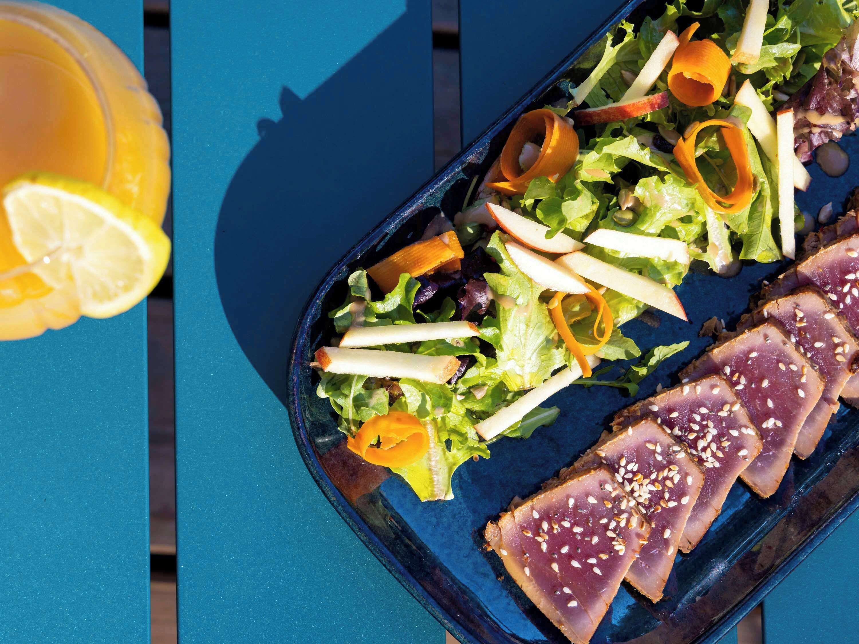 Un plato de sashimi y ensalada sobre una mesa azul.