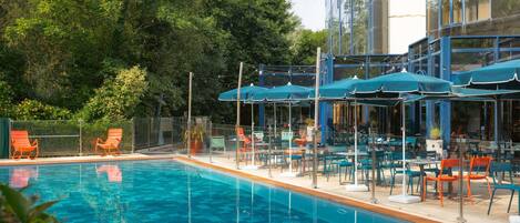 Ein Pool mit Liegestühlen und Sonnenschirmen, umgeben von Grünpflanzen und einem modernen Gebäude.