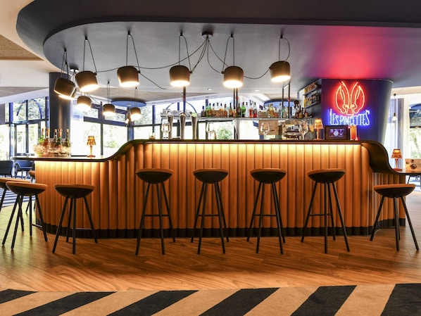 Un espace bar agrémenté d’un néon, d’un comptoir en bois, de tabourets et offrant une vue sur l’extérieur grâce à de grandes fenêtres.