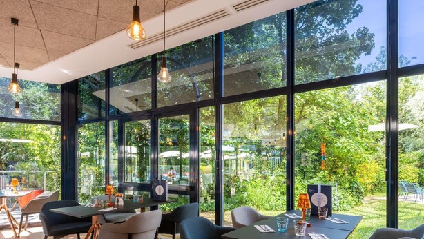 An indoor dining area with large windows, modern furniture, and a view of the outdoors.