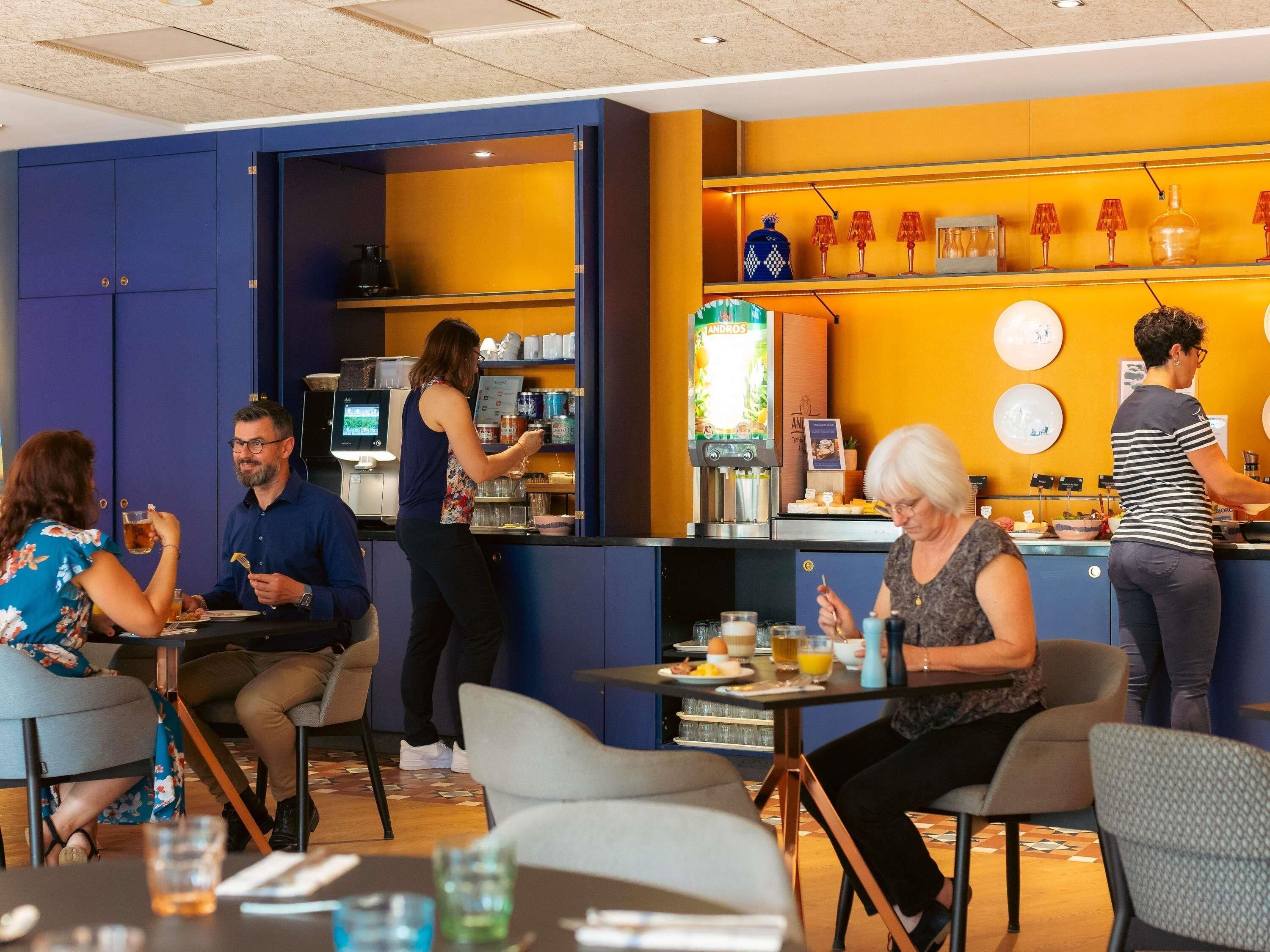 A cafe with tables and chairs, a coffee machine, and a counter where a person is preparing food.