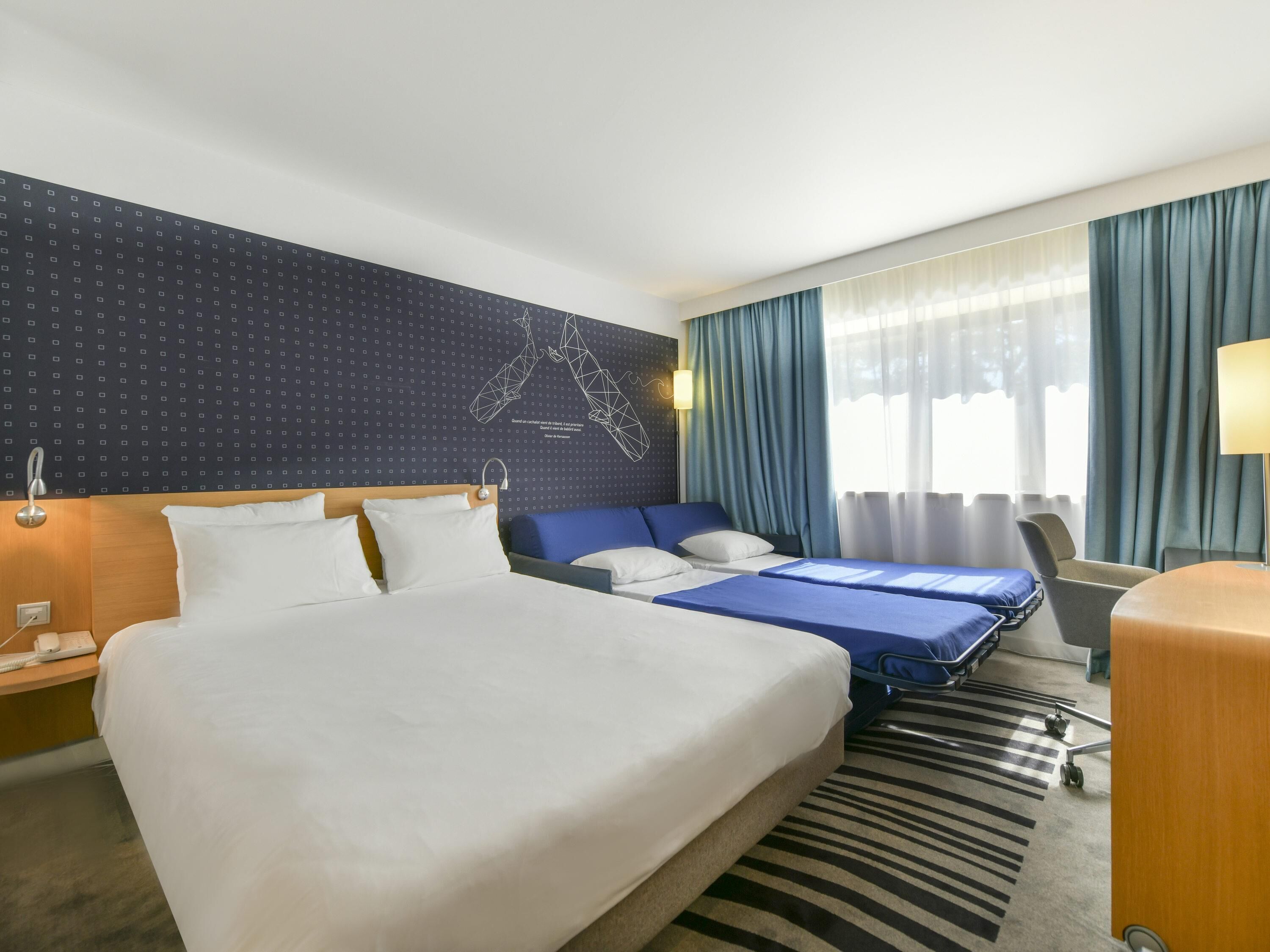 A hotel room with a large bed, a smaller bed, a desk, and a chair.