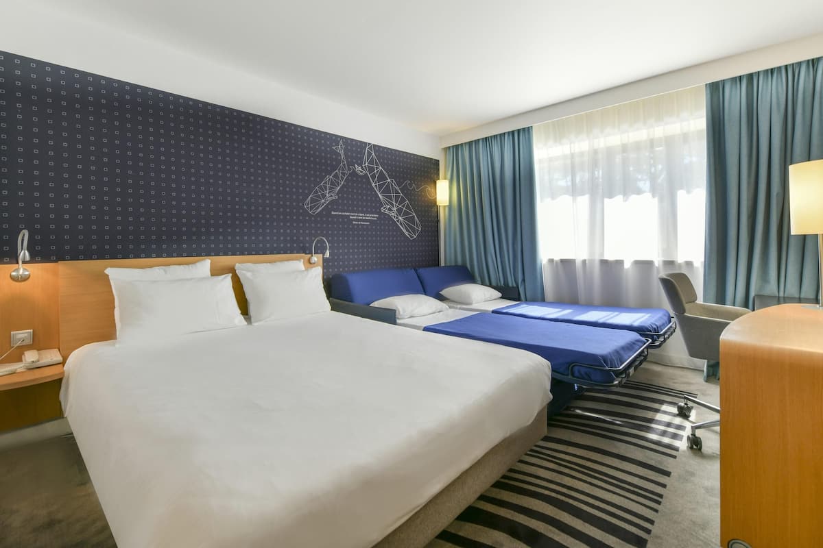 A hotel room with a large bed, a smaller bed, a desk, and a chair.