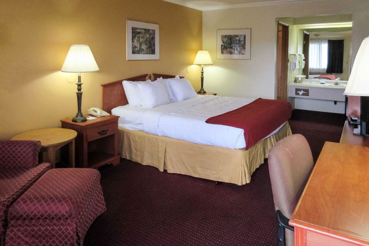 A hotel room with a bed, two bedside lamps, a desk, a chair, and a mirror.