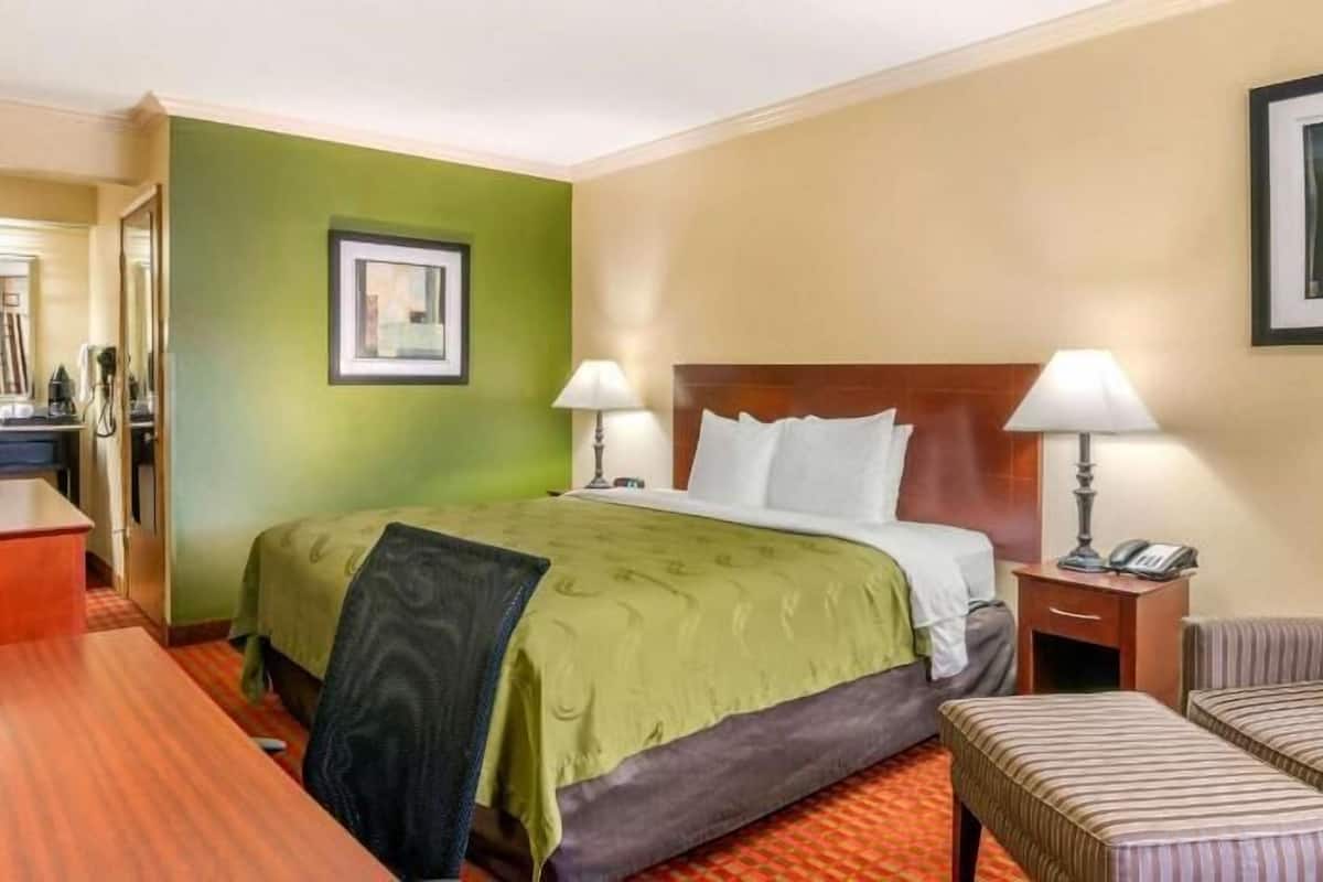 A hotel room with a bed, a desk, a chair, a nightstand, and a television.
