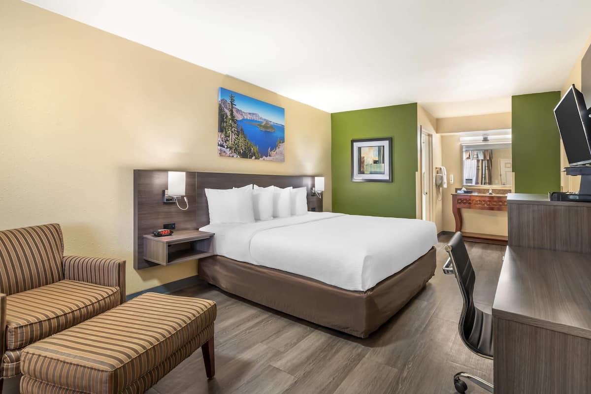 A hotel room with a large bed, a desk, a chair, a small sofa, and a painting on the wall.