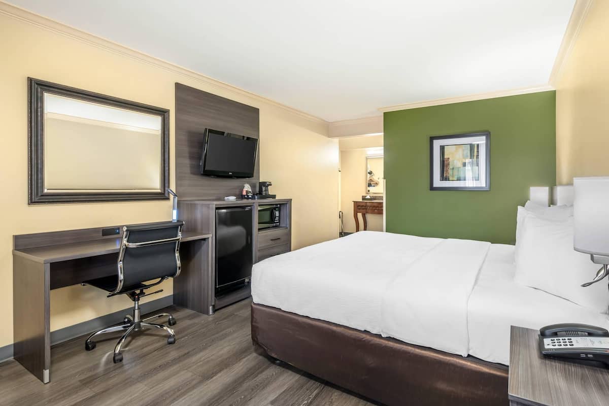 A hotel room with a large bed, a desk with a chair, a television, and a coffee machine.