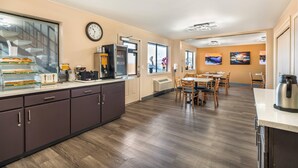 A modern kitchen with a built-in oven, microwave, and coffee maker. There is a dining area with wooden tables and chairs. - Quality Inn Klamath Falls - Crater Lake Gateway (Klamath Falls)