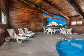 A wooden cabin interior with a pool, lounge chairs, and a mural of a mountain scene.