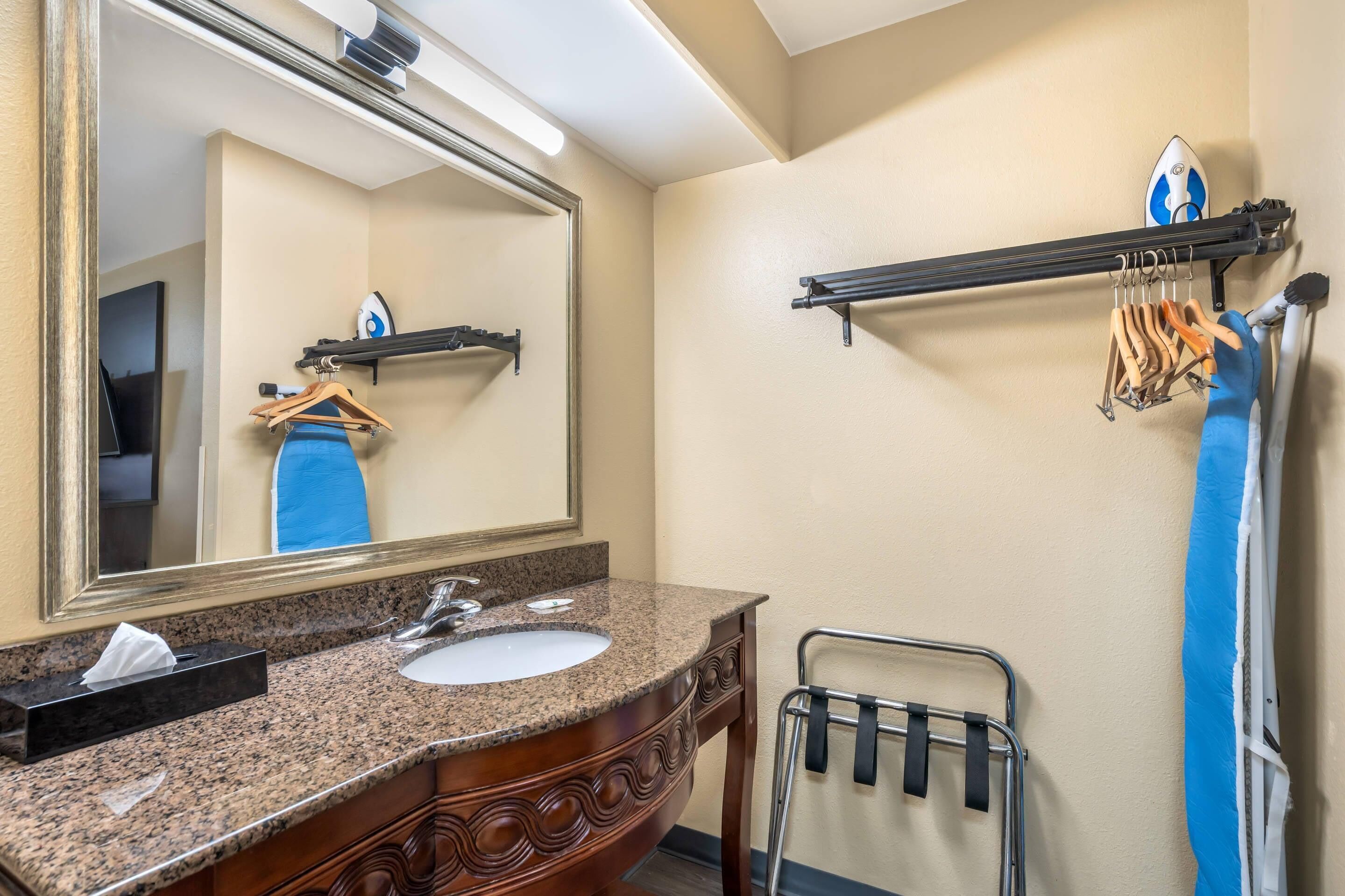 A bathroom with a granite countertop sink, a mirror, a towel rack, and a towel rack with hangers.