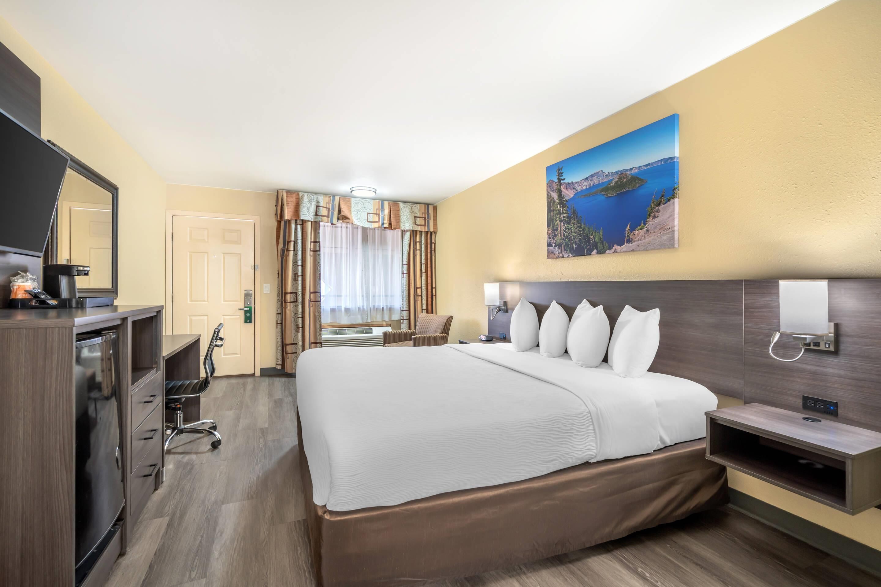 Ein Hotelzimmer mit einem großen Bett, einem Schreibtisch mit Stuhl, einem Fernseher und einem Bild an der Wand.