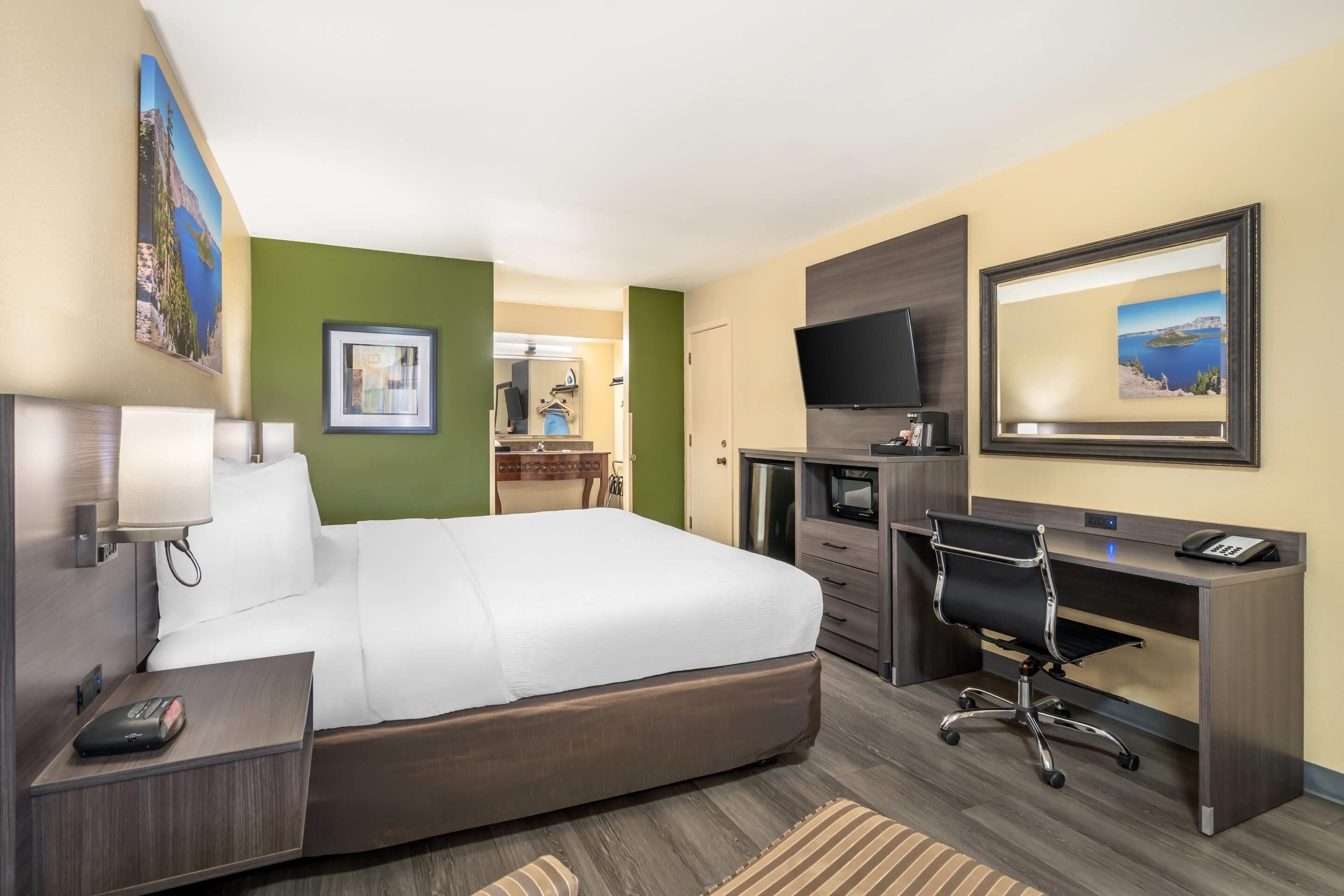 A hotel room with a bed, desk, TV, and a view of the sea.