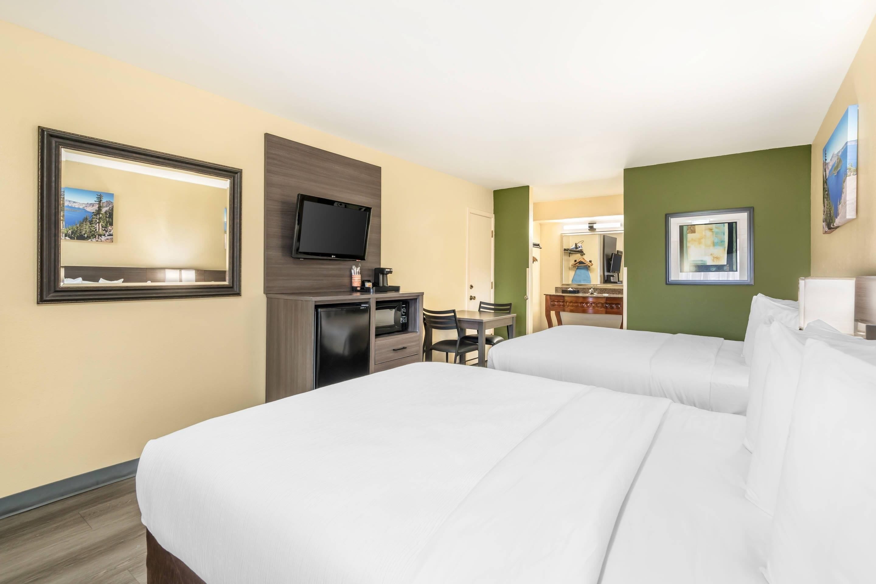 Hotellihuone, jossa on kaksi sänkyä, työpöytä tuolilla, televisio ja kahvinkeitin.