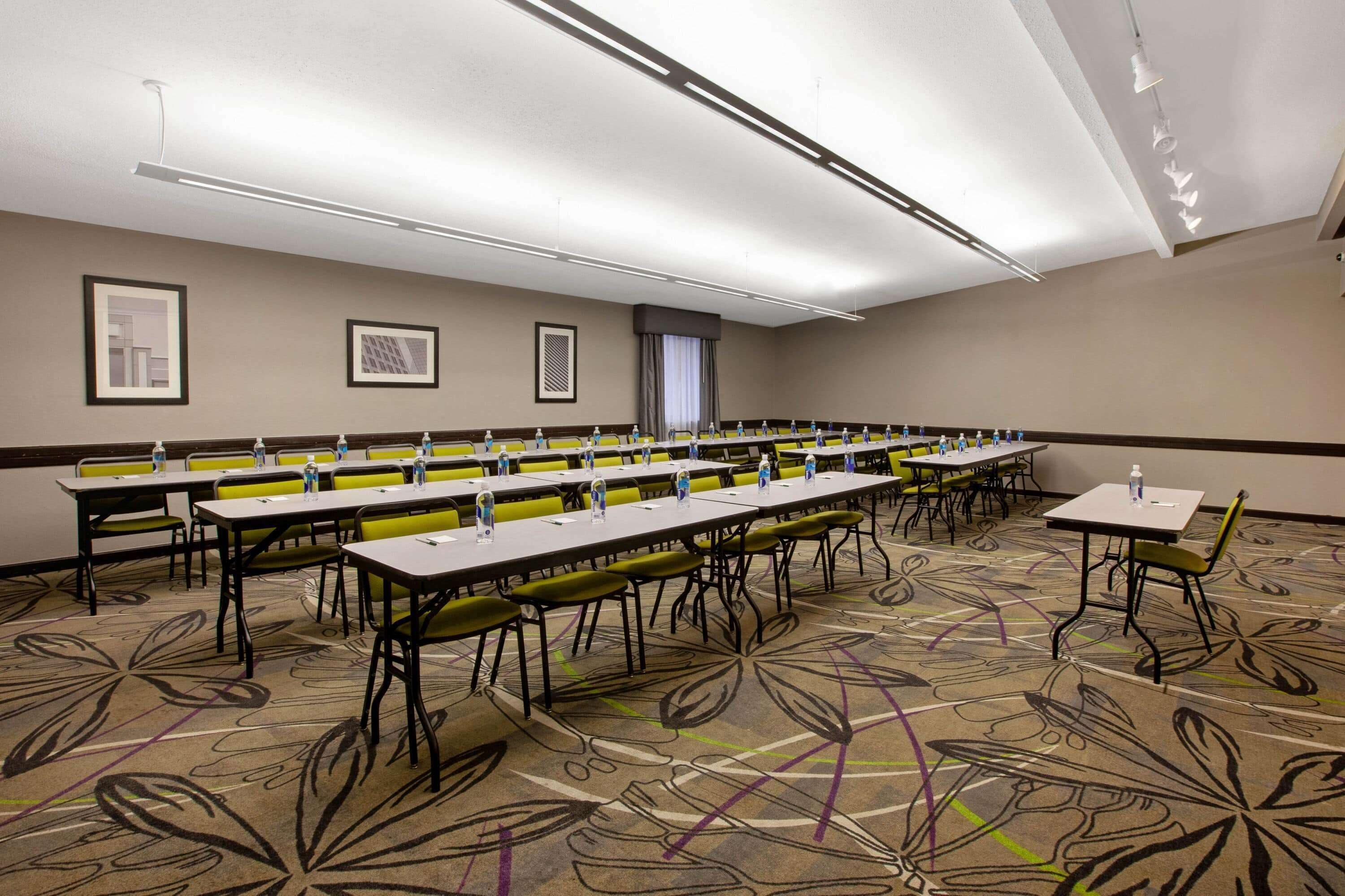 A conference room with long tables, yellow chairs, and a patterned carpet.