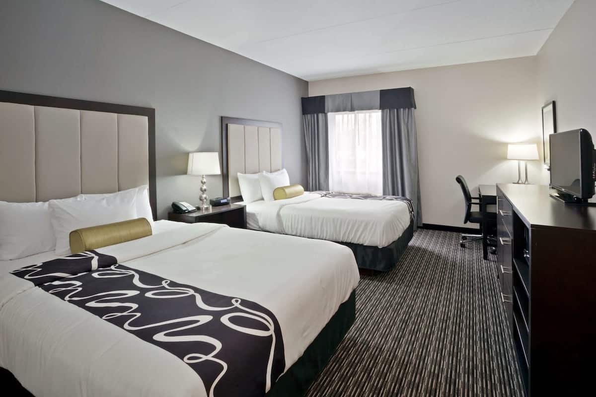 Ein Hotelzimmer mit zwei Betten, einem Schreibtisch, einem Stuhl, einem Fernseher und einer Lampe.