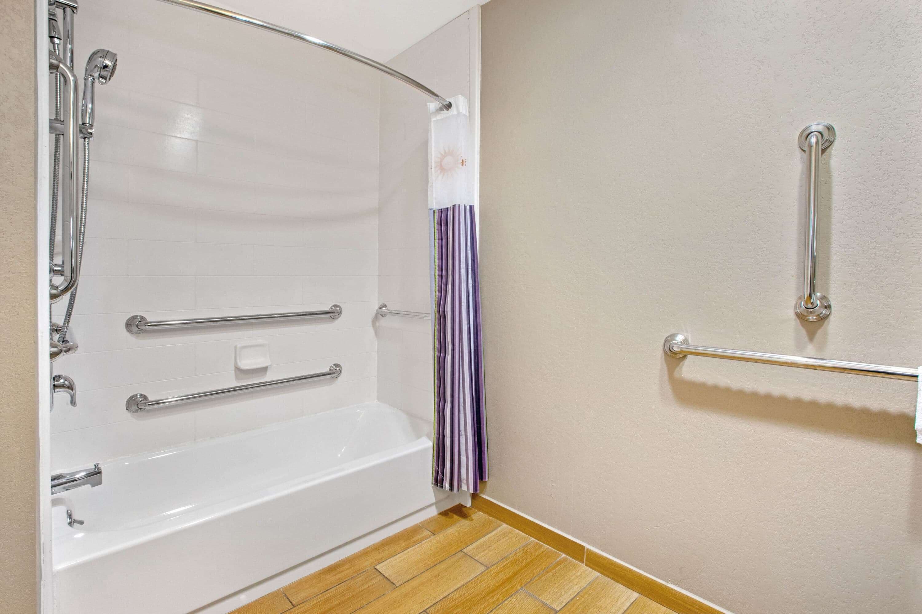 Un baño con una bañera blanca, barras de apoyo y una ducha con cortina.