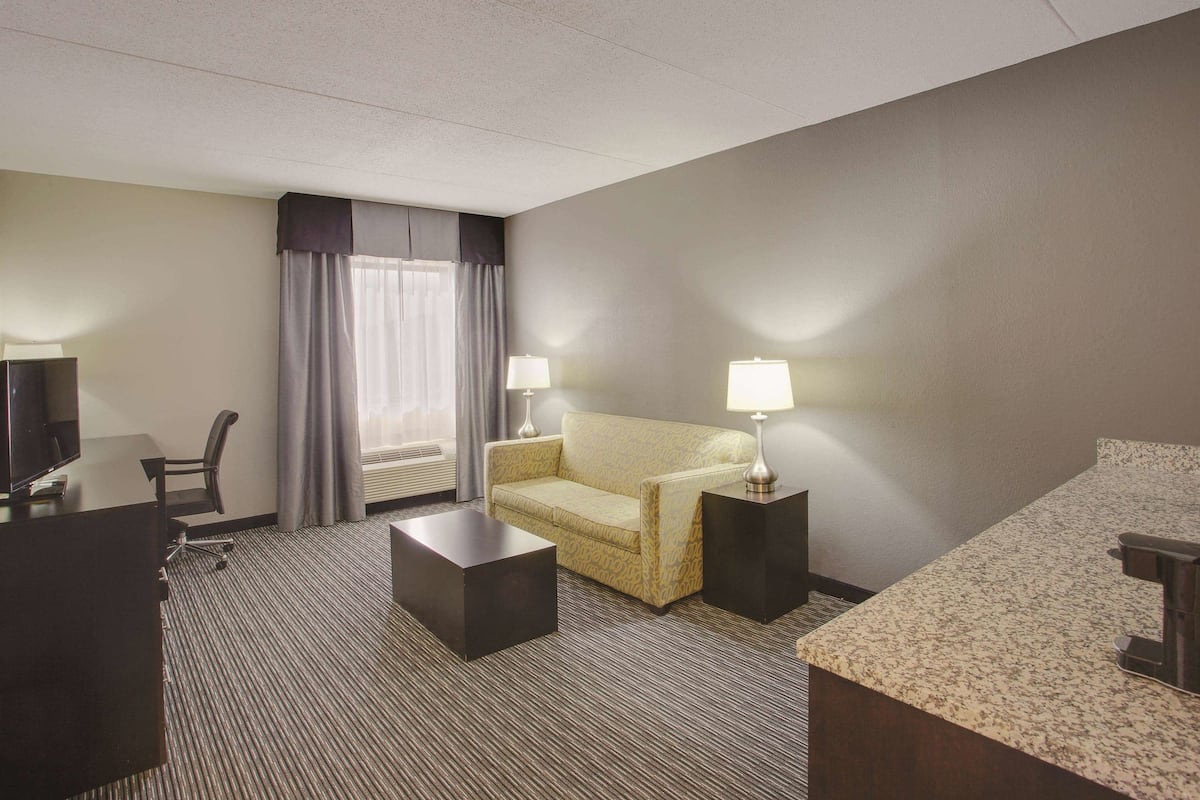 Ein Hotelzimmer mit Bett, Sofa, Schreibtisch, Sessel, Couchtisch und zwei Lampen.
