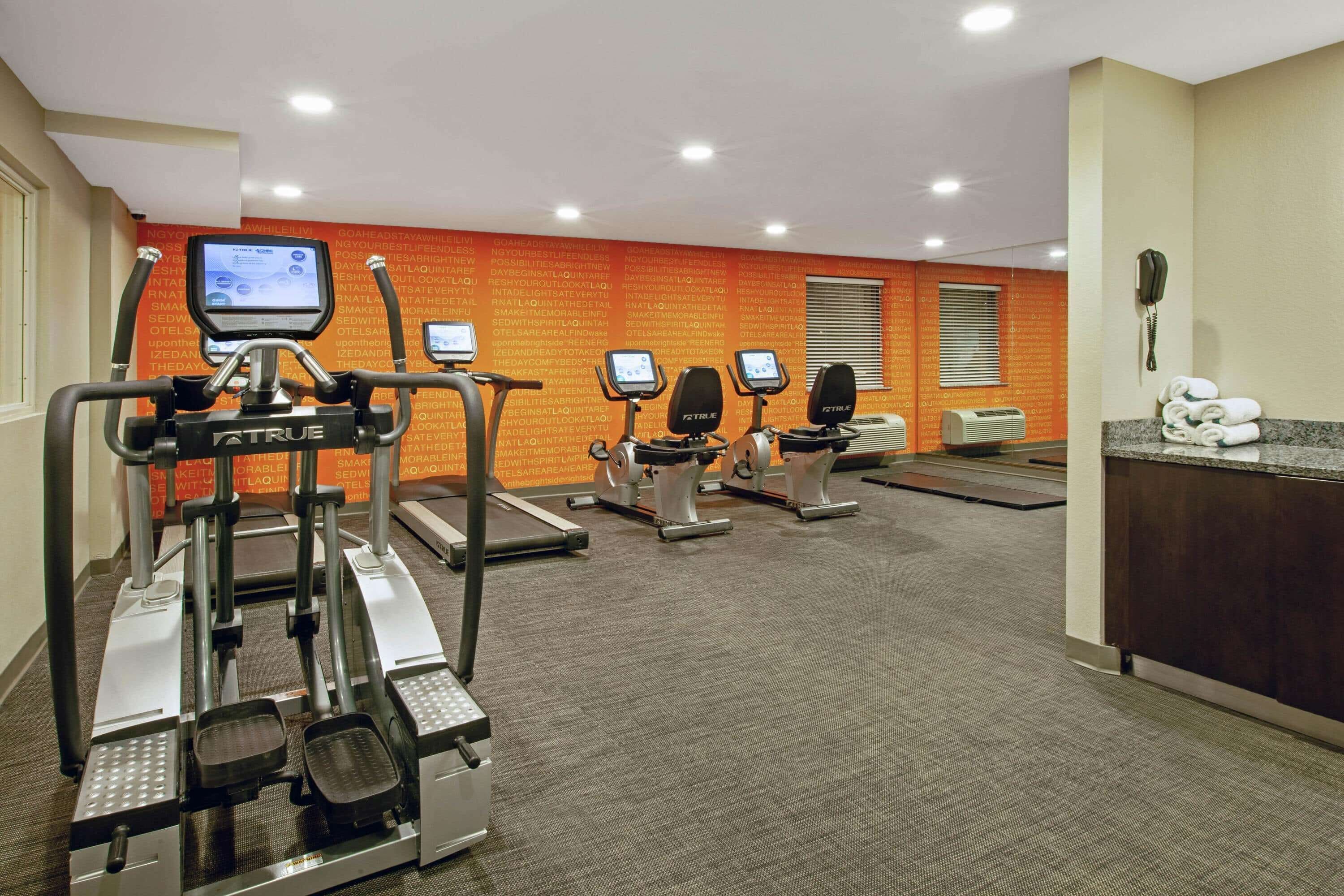 Ein Fitnessstudio mit Laufbändern, Crosstrainern und einem digitalen Bildschirm.