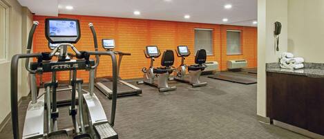 Ein Fitnessstudio mit Laufbändern, Crosstrainern und einem digitalen Bildschirm.