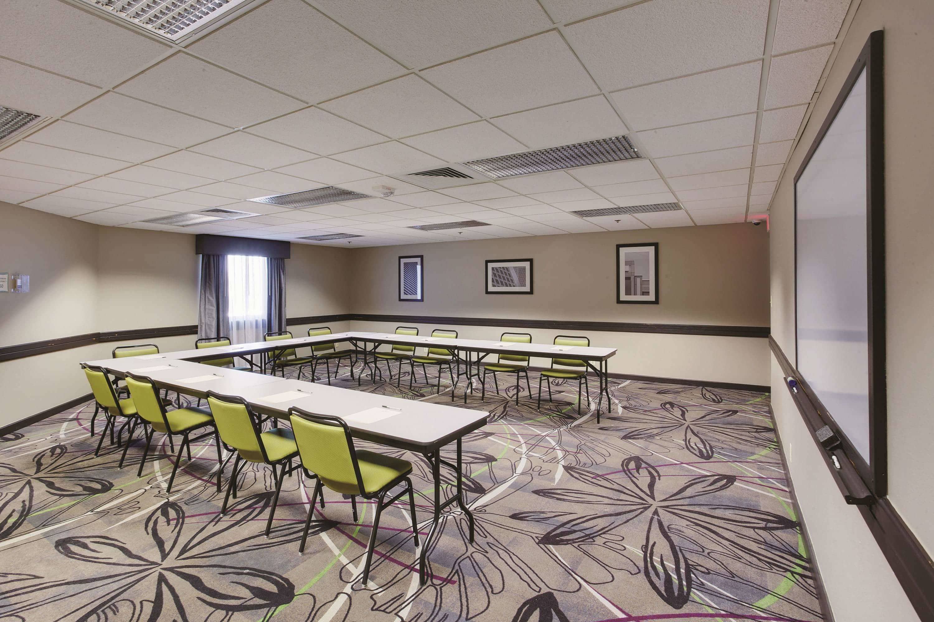 A conference room with a long table and chairs, a projector screen, and patterned carpet.