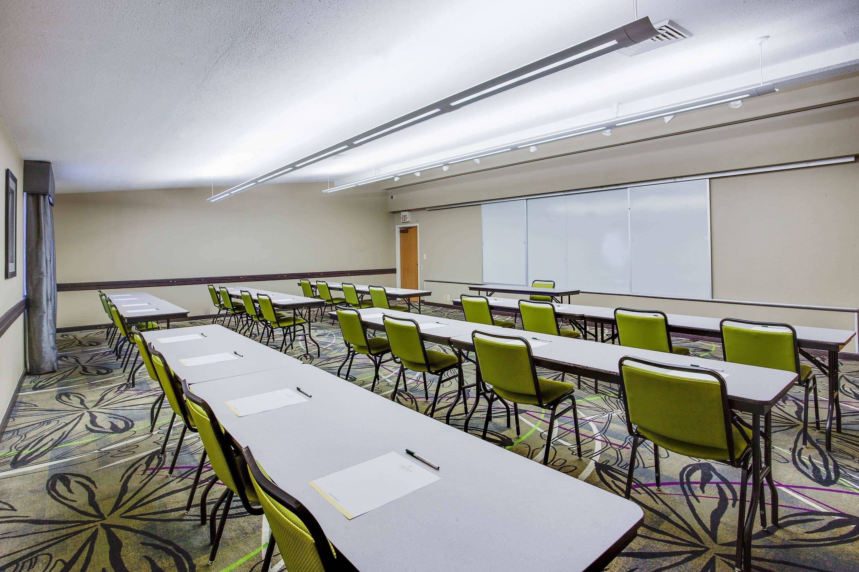 A conference room with long tables and chairs, a whiteboard, and a carpeted floor.