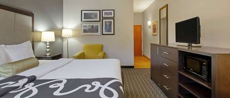 A hotel room with a large bed, a television, a microwave, a chair, and a dresser.