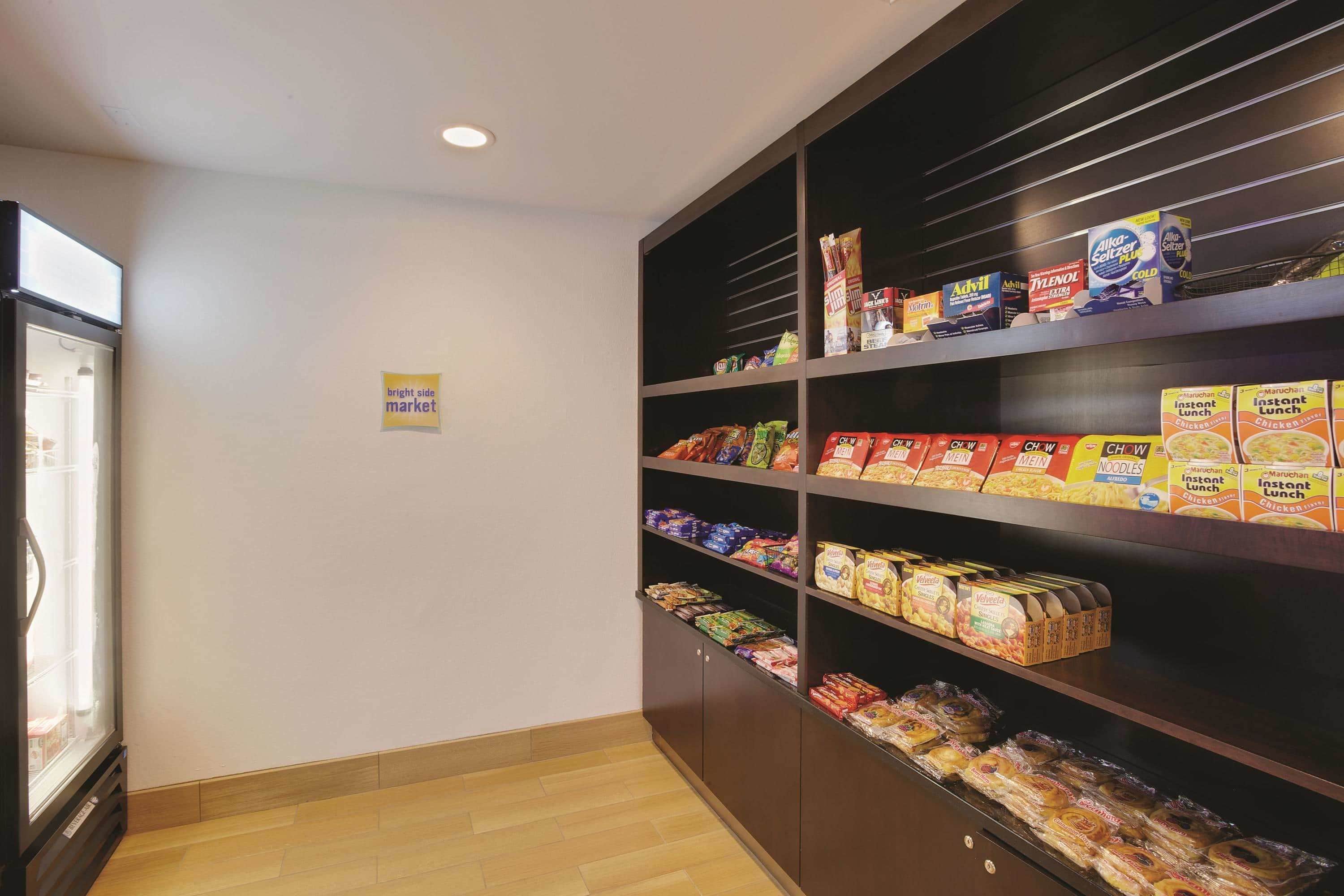 A kitchenette with a refrigerator, shelves stocked with various food items, and a sign indicating a bright side market.