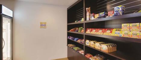 A kitchenette with a refrigerator, shelves stocked with various food items, and a sign indicating a bright side market.