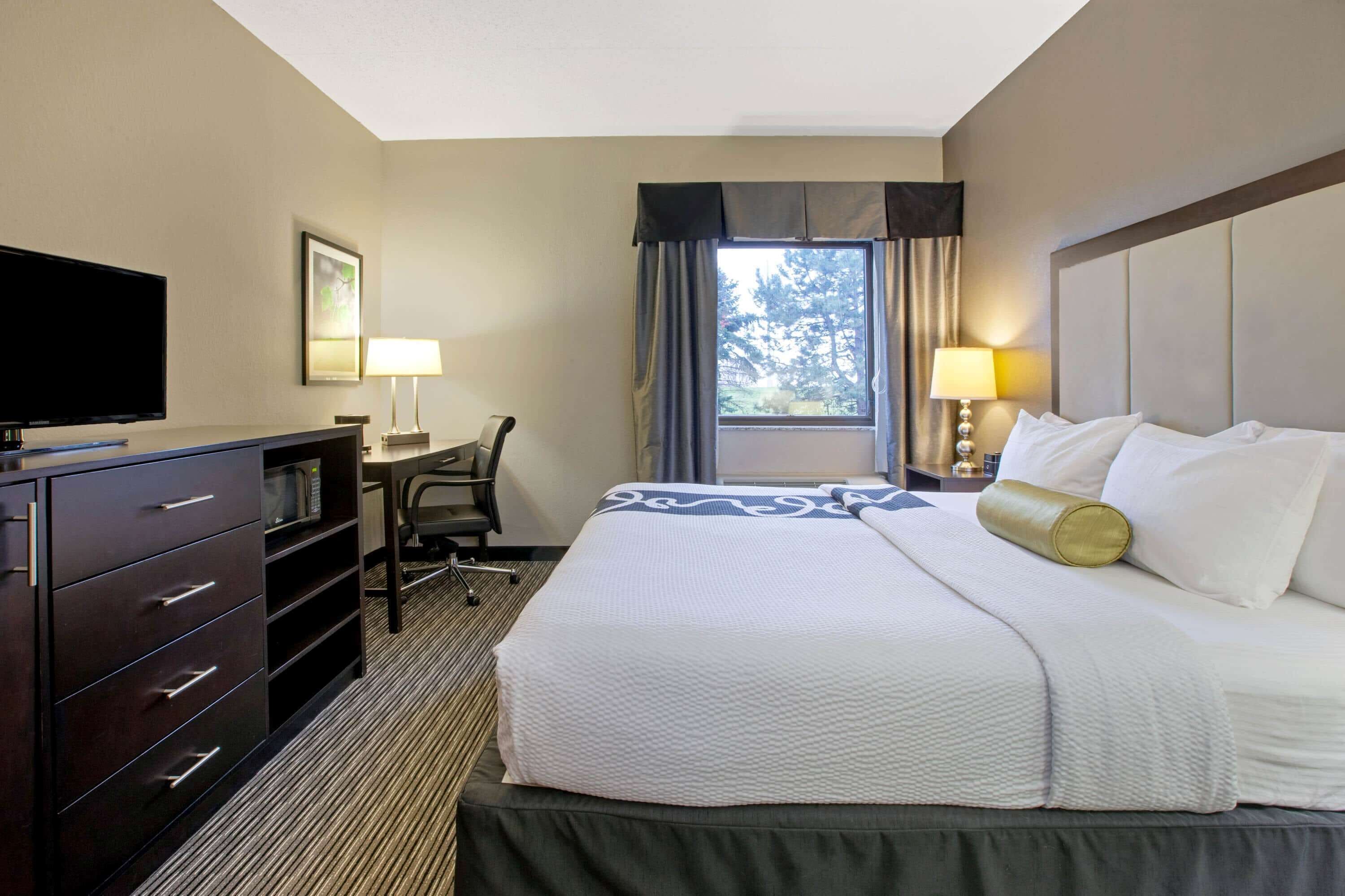 A hotel room with a bed, a desk, a television, and a window with curtains.