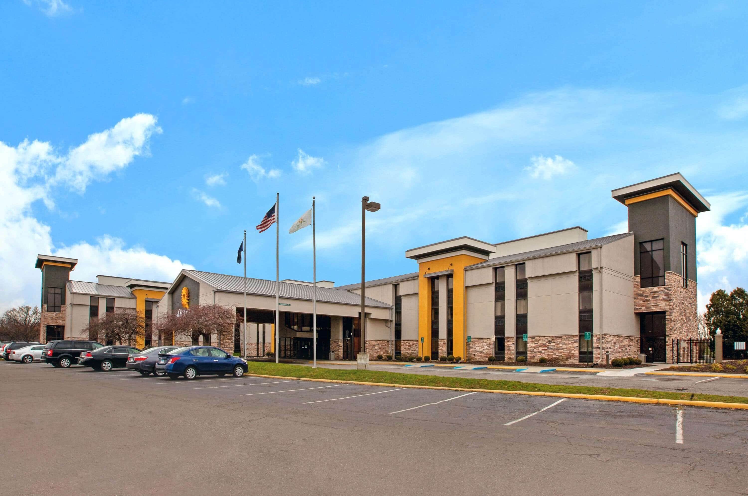 A modern building with a parking lot, multiple flags, and a clear sky.