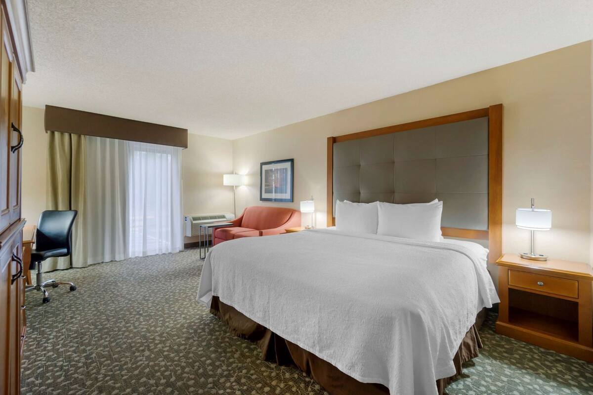 A hotel room with a large bed, a desk, a chair, and a window with curtains.