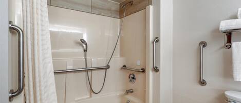 A modern bathroom with a bathtub, shower, and toilet. It includes grab bars and a towel rack.