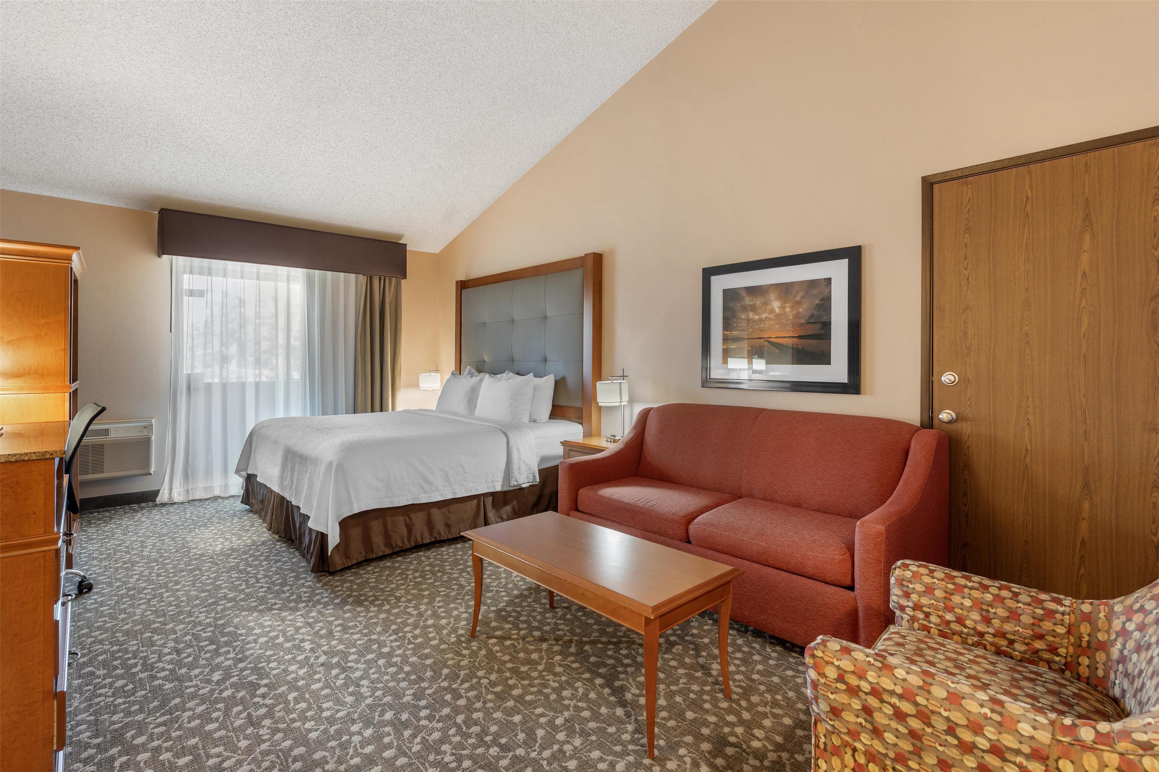 A hotel room with a bed, a sofa, a coffee table, a desk, and a picture on the wall.