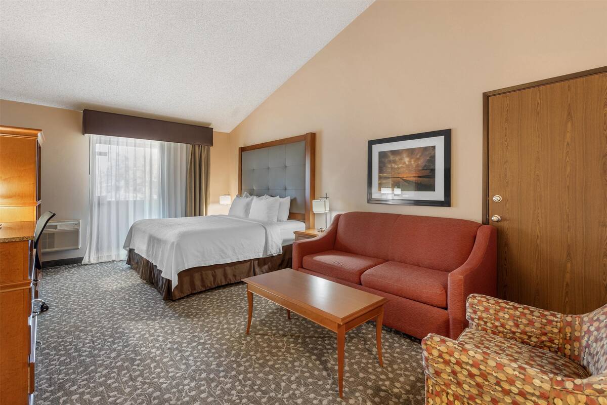 A hotel room with a bed, a sofa, a coffee table, a desk, and a picture on the wall.