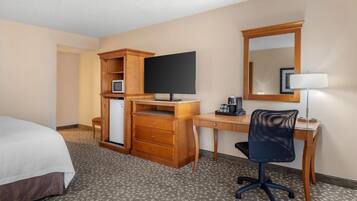 Habitación de hotel con cama, escritorio, computadora, silla, televisor, espejo y lámpara.