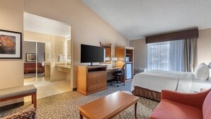 Habitación de hotel con cama, escritorio, televisor, armario y baño visible a través de una puerta abierta.