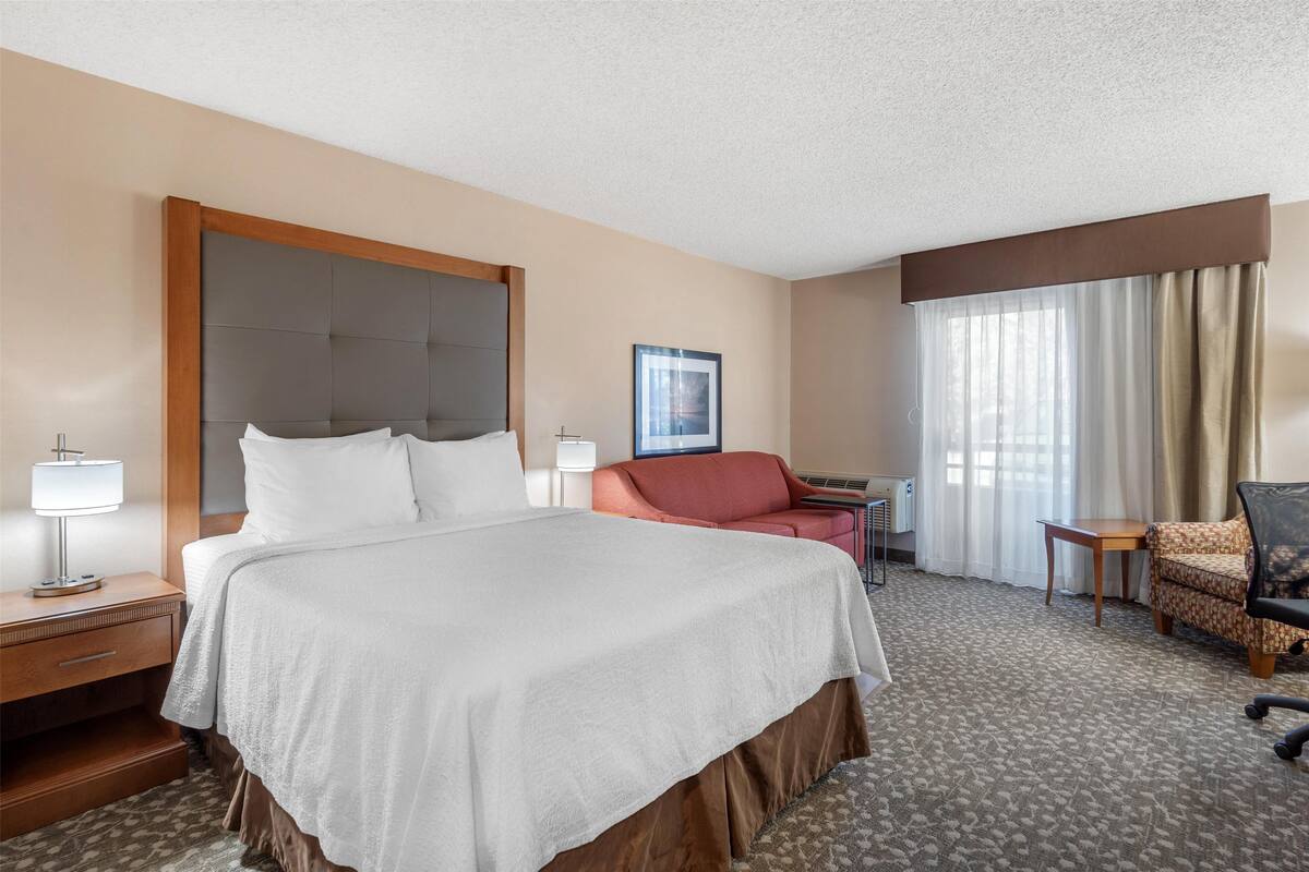 A hotel room with a large bed, a desk, a chair, and a window with curtains.