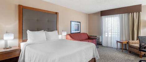 Habitación de hotel con una cama grande, un escritorio, una silla y una ventana con cortinas.